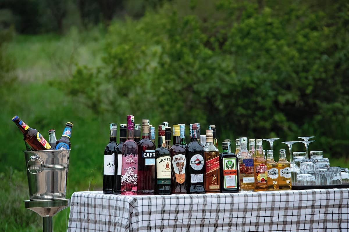A variety of liquor bottles and glasses on a table outdoors.