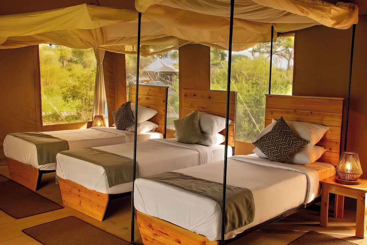 A tented accommodation with two wooden beds, each with a pillow and a bedside lamp.