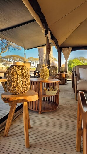 A tented outdoor seating area with wooden furniture, woven decorative items, and a view of the landscape. - Tarangire Greenland Retreat (Tarangire National Park)