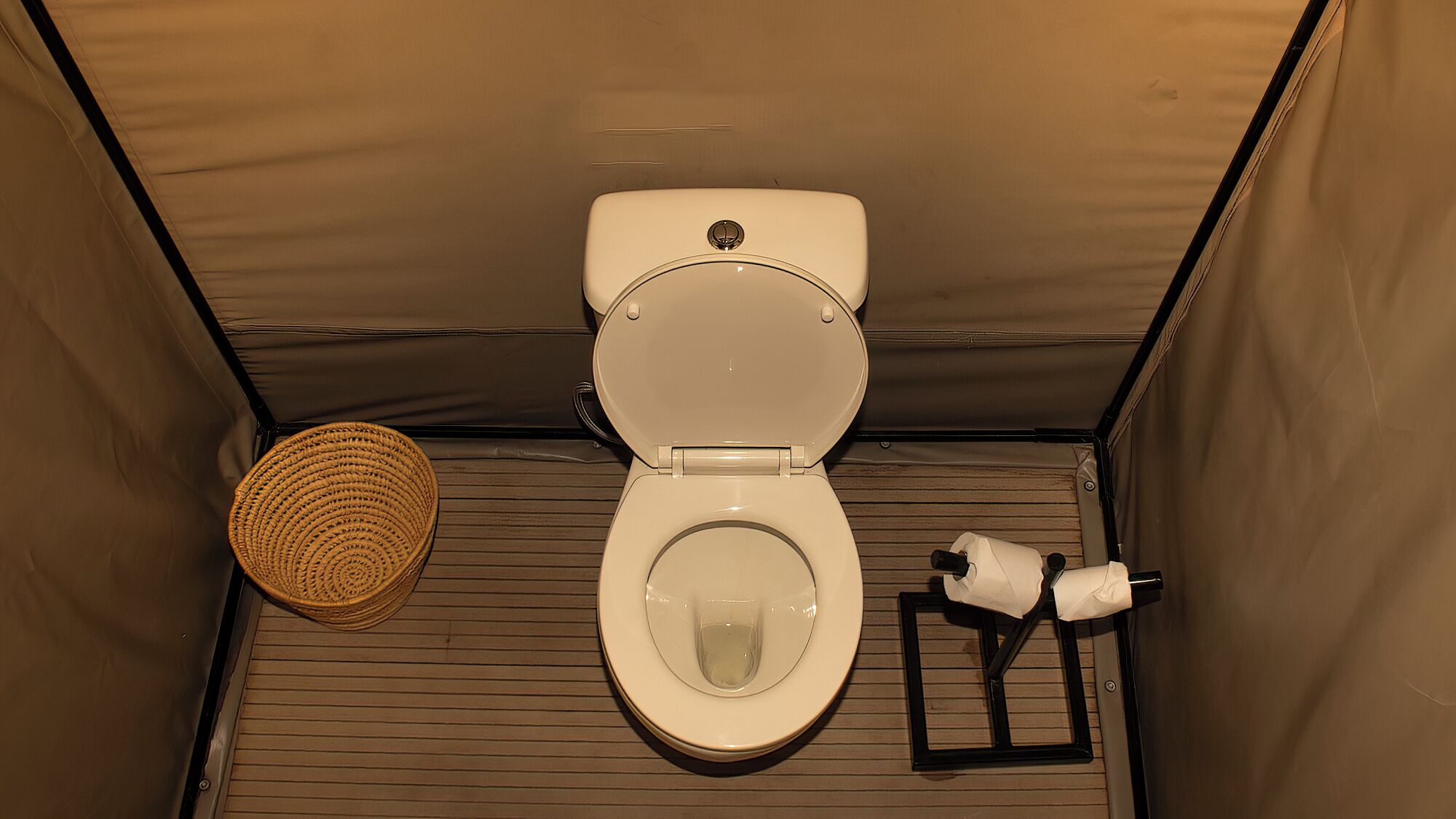 Un baño pequeño y cerrado con inodoro, un estante con artículos de aseo y un tapete tejido en el suelo.