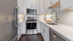 A modern kitchen with white cabinetry, stainless steel appliances, and a wooden countertop.