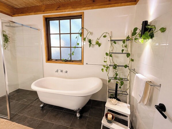 A bathroom with a freestanding bathtub, a glass shower enclosure, a window with a view, and a plant wall.
