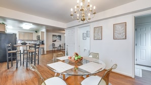 A modern kitchen with wooden cabinets, a black refrigerator, and a dining area with a glass table and white chairs. - 1 Mi to Colonial Beach Boardwalk! Cozy Family Home (Colonial Beach)