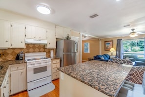 A compact kitchen with a gas stove, oven, and refrigerator, a dining area with a table and chairs, and a living room with a sofa and a window. - Over The Hill By The Bayou, Pool, Family Friendly (Pensacola)