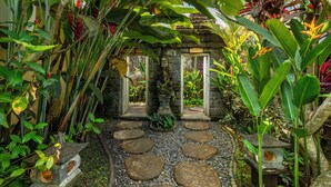 A stone pathway leading to a stone structure with a lantern, surrounded by lush tropical plants. - Belas Vana Villa Ubud by Dhananjaya Hospitality (Sebatu)