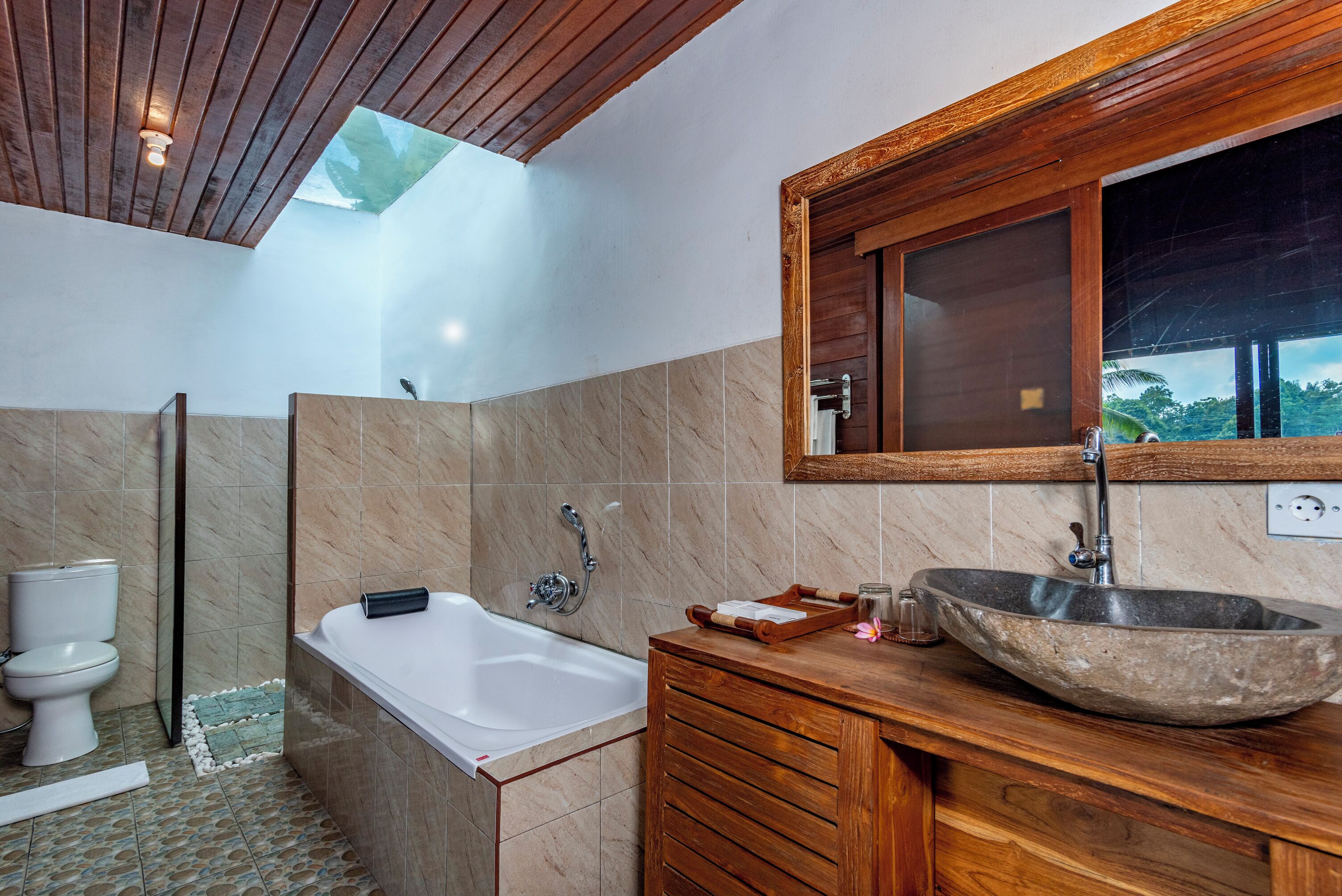 Een moderne badkamer met een badkuip, een houten wastafelmeubel, een ruime stenen wasbak en een dakraam boven de douche.