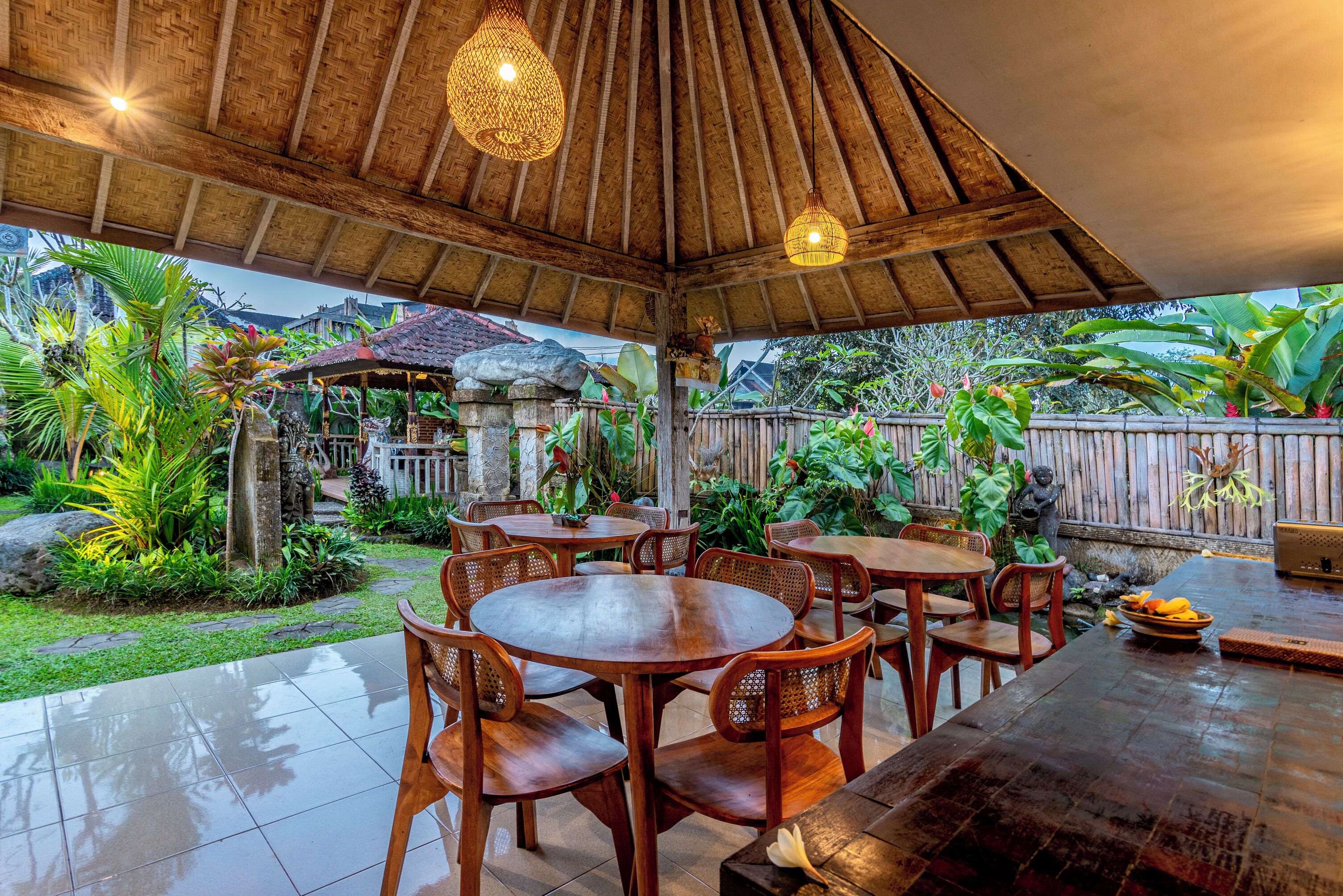 Eine Terrasse im Freien mit Holztischen und -stühlen, umgeben von üppiger Bepflanzung und einem Reetdach.