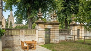 A courtyard with a stone gate, a wooden table with chairs, and a paved path. - The Gate House (Apethorpe)