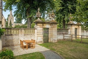 A courtyard with a stone gate, a wooden table with chairs, and a paved path. - The Gate House (Apethorpe)