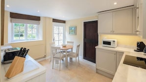 A compact kitchen with white cabinets, a dining table with chairs, a microwave, and a coffee machine. - The Gate House (Apethorpe)