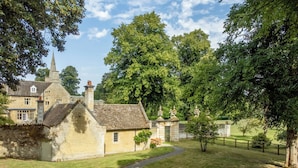 A traditional stone building with a prominent tower, surrounded by lush greenery and a well-maintained lawn. - The Gate House (Apethorpe)