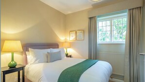 A hotel room with a large bed, two bedside tables with lamps, a window with curtains, and framed pictures on the wall. - The Gate House (Apethorpe)