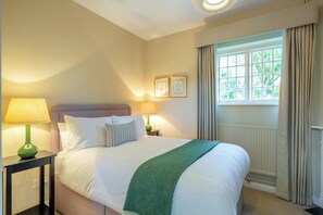 A hotel room with a large bed, two bedside tables with lamps, a window with curtains, and framed pictures on the wall. - The Gate House (Apethorpe)