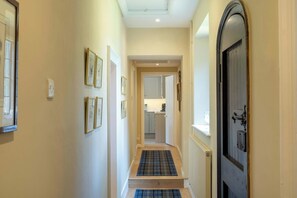 A narrow hallway with framed pictures on the walls, a blue and black plaid mat at the entrance, and a door on the right. - The Gate House (Apethorpe)