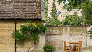 A brick wall with climbing plants and a small table with chairs. - The Gate House (Apethorpe)