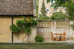 A brick wall with climbing plants and a small table with chairs. - The Gate House (Apethorpe)
