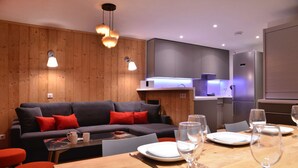 A modern living room with a sofa, red cushions, and a wooden dining table set for a meal. - Belle Plagne Premium : ski in & out / 8 personnes (MACOT LA PLAGNE)