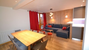 A modern living room with a wooden floor, a grey sofa with red cushions, a wooden dining table with chairs, and a glass coffee table. - Belle Plagne Premium : ski in & out / 8 personnes (MACOT LA PLAGNE)