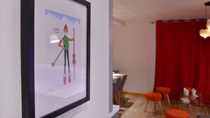 A framed picture of a skier on a wall, a dining area with chairs and a table, and a red curtain in the background. - Belle Plagne Premium : ski in & out / 8 personnes (MACOT LA PLAGNE)