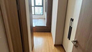 A narrow hallway with wooden flooring, a sliding door on the right, and a window at the end. - Oanh Luxstay (Bac Hong Linh)