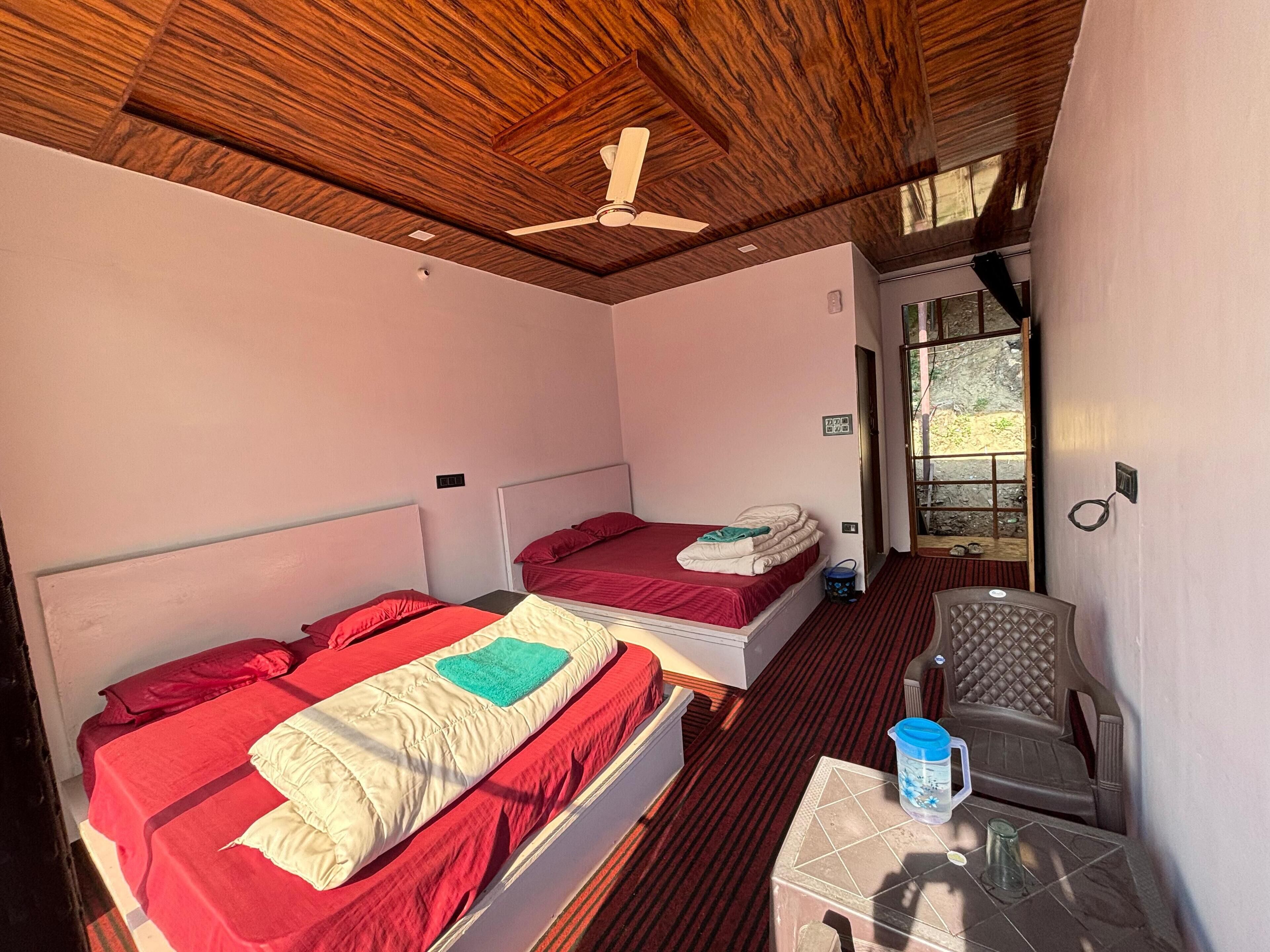 A room with two beds, a ceiling fan, a window, and a small table with a water bottle.