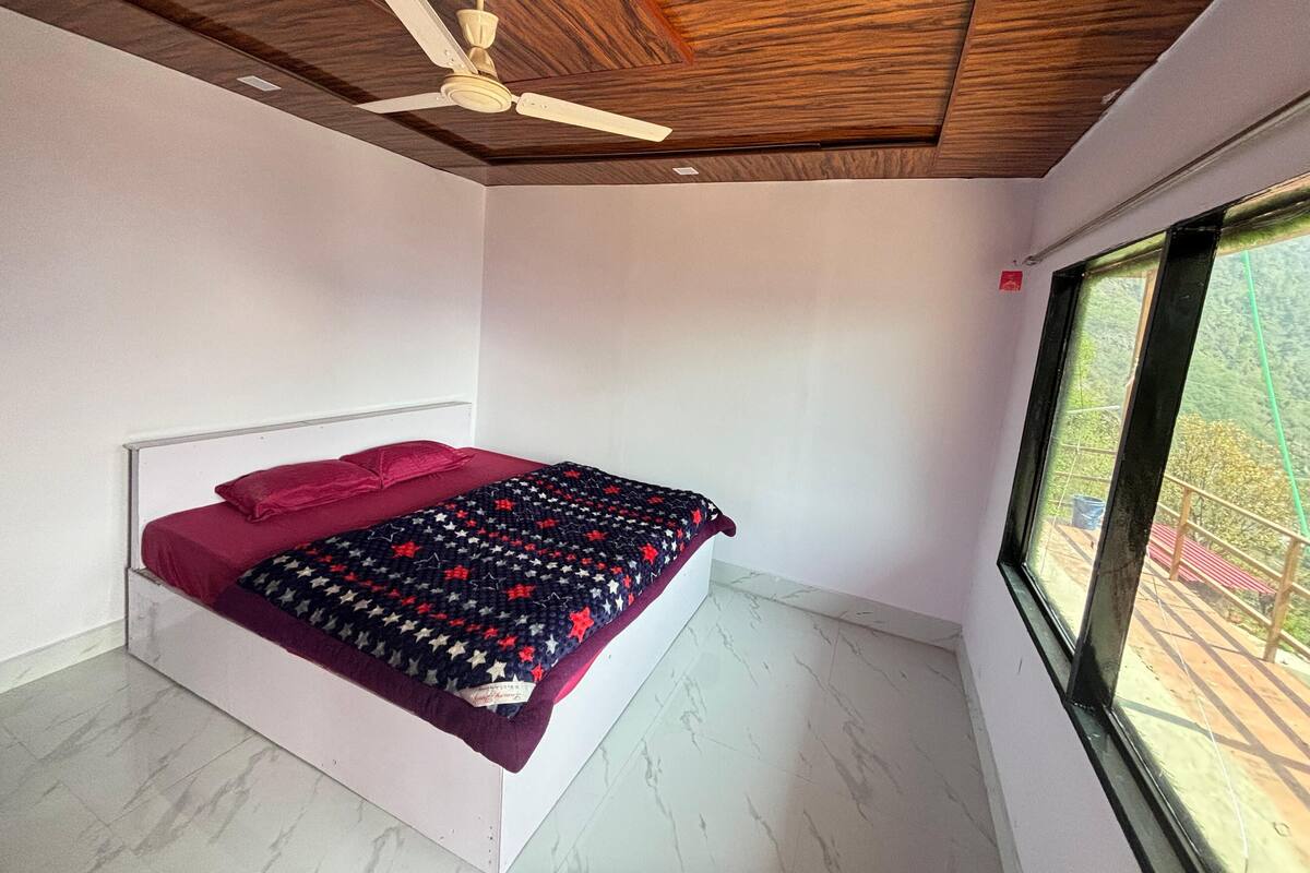 Un dormitorio con cama, ventilador de techo, ventana y vistas al exterior.