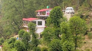 A multi-story building with a red roof, surrounded by dense greenery and hills in the background. - Kedar Hill Resort  (Ukhimath)