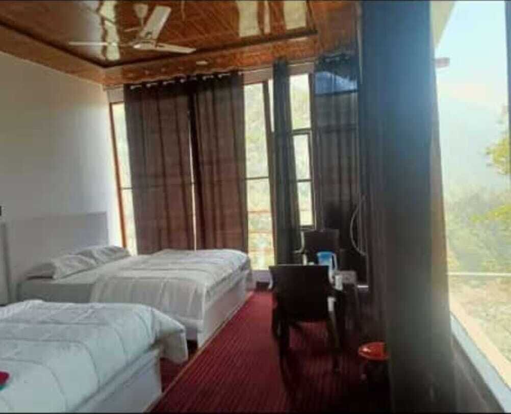 A hotel room with two beds, a desk, and a view of the outdoors.
