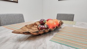 Una mesa de comedor con un cuenco de madera lleno de frutas, un mantel a rayas y un cuadro en la pared.