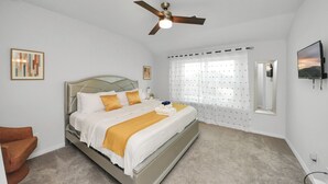 Un dormitorio con cama, ventilador de techo, televisor y ventana con cortinas.