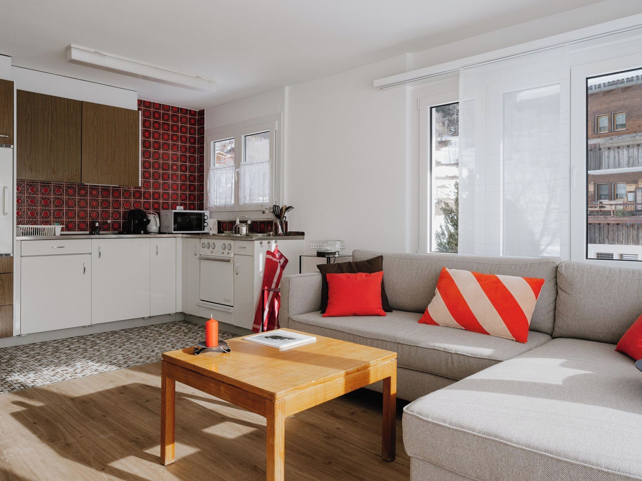 A modern kitchen with white cabinets, a red patterned backsplash, and a microwave.