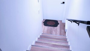 A staircase with wooden steps and metal railings, leading to a door with a doormat.