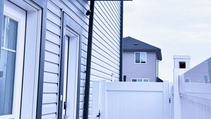 A residential building with a garage door, a white fence, and a house in the background.