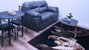 A modern living room with a grey leather sofa, a round table with chairs, a small side table with a vase, and a large wall painting of swans.
