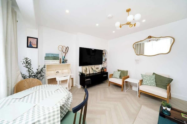 A modern living room with a flat-screen TV, a sofa, a dining table, and a decorative mirror.