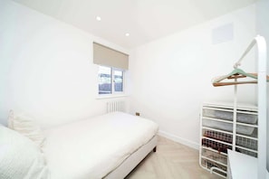 A bedroom with a bed, a window, and a white storage unit with shelves.