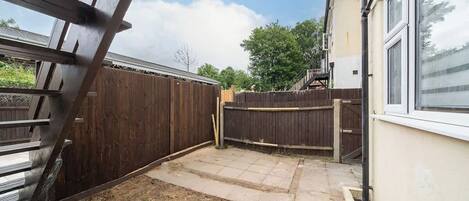 A backyard with a wooden fence, a concrete patio, and a house with a window.