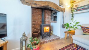 A cozy living room with a brick fireplace, a television, and a bookshelf. - Modern Snitton Cottage & Gardens (Snitton)