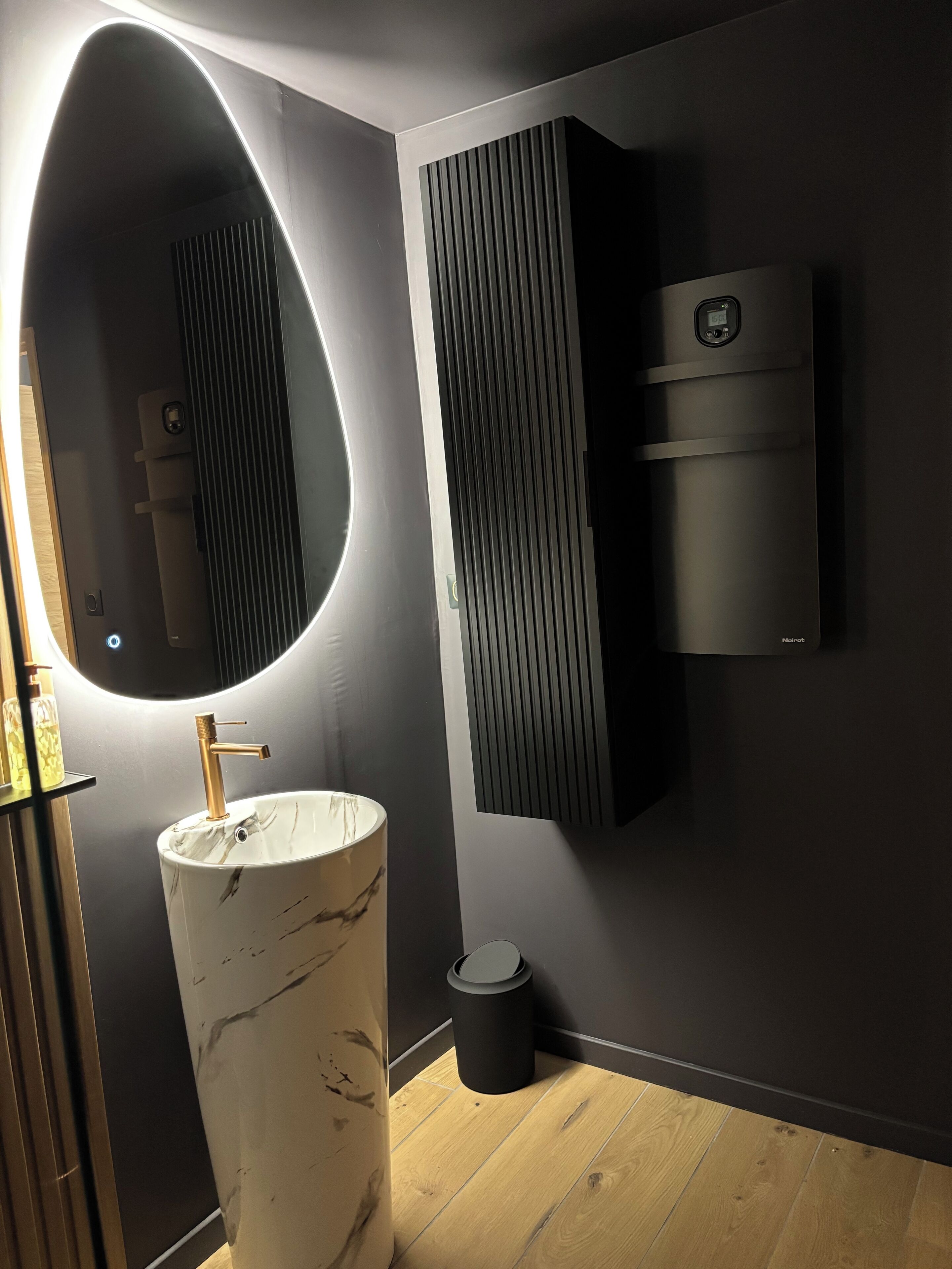 Een moderne badkamer met een marmeren wastafel, een spiegel aan de muur en een zwarte handdoekwarmer.