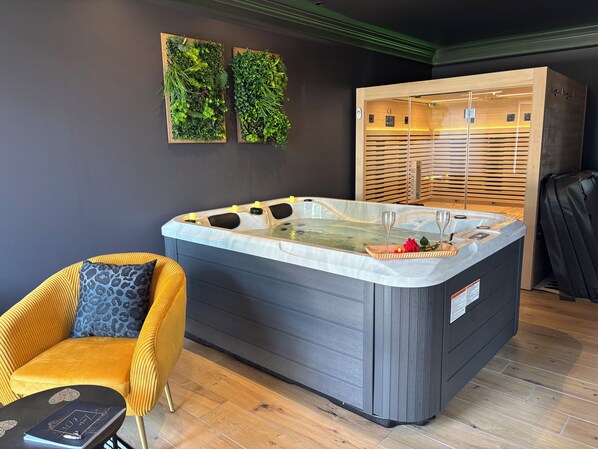 A modern spa room with a large hot tub, a yellow chair, and two wall-mounted green plant displays.