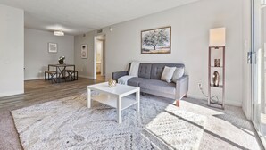 Ett modernt vardagsrum med en grå soffa, ett vitt soffbord och en mönstrad matta.