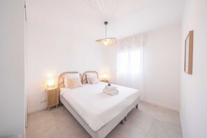 Una camera da letto con un letto, lampade da comodino, un lampadario e una finestra con tende.