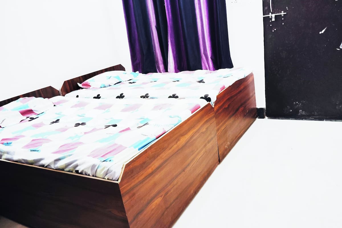 A wooden bed with a patterned bedspread in a room with a black door and purple curtains.
