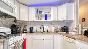 Une cuisine moderne avec des meubles blancs, une cuisinière à gaz, un lave-vaisselle et un plan de travail en granit.