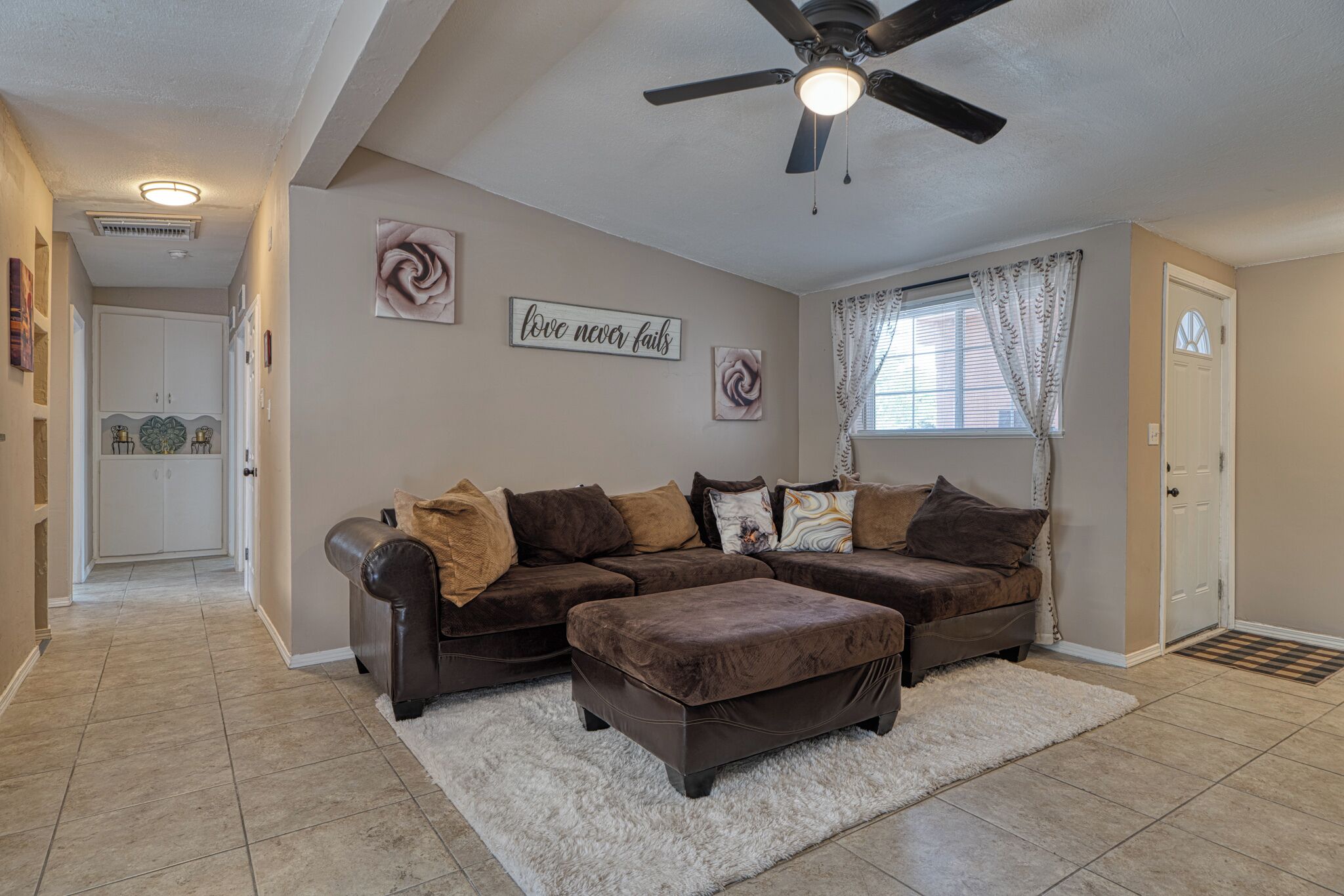 A living room with a sectional sofa, a ceiling fan, and a rug.