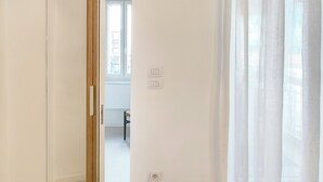 A minimalist room with a large mirror, a wooden door, and a window with sheer curtains. - Piano 7 | Bright penthouse with terrace (Torino)
