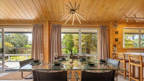 A dining area with a glass table, leather chairs, and a wooden ceiling. - 5 minutes walk to beautiful beach & shops, fully fenced section pet friendly. (Matarangi)