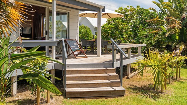 A house with a covered porch, outdoor seating, and a staircase leading to the entrance. - 5 minutes walk to beautiful beach & shops, fully fenced section pet friendly. (Matarangi)