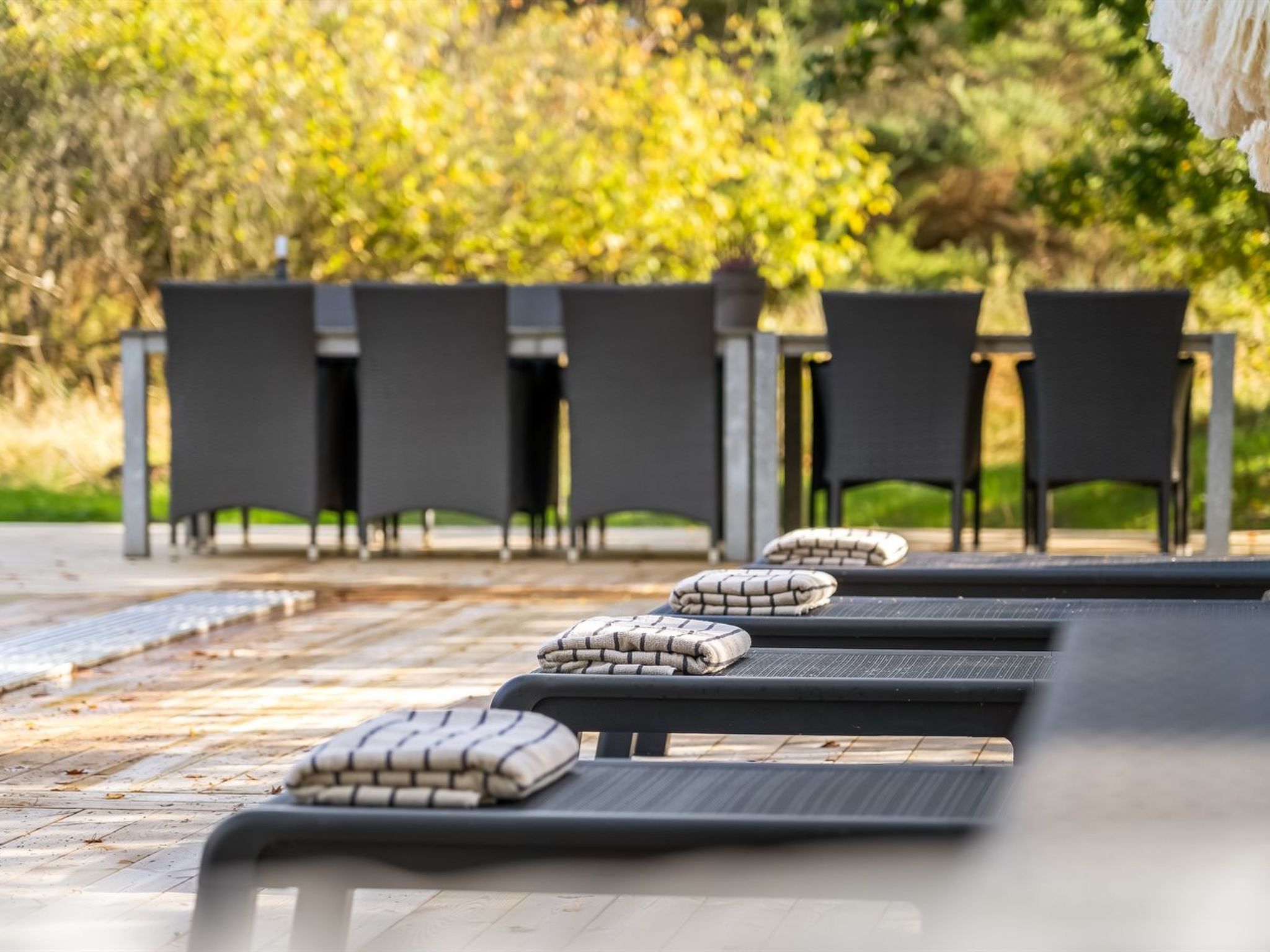 Una hilera de sillones de relax con cojines, una mesa y sillas en un entorno al aire libre.
