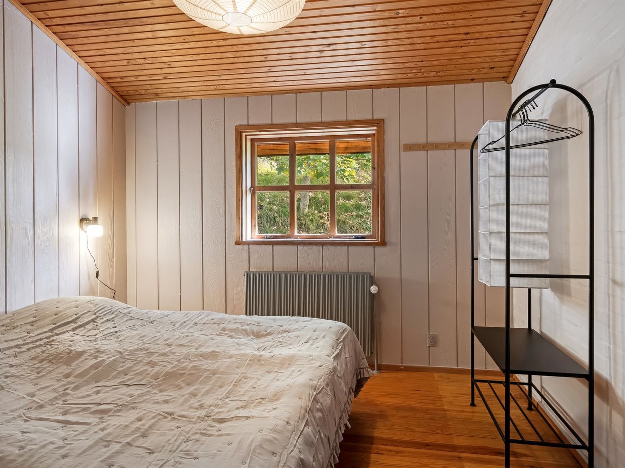 Une chambre à coucher avec un lit, une fenêtre, un radiateur et une étagère en métal.